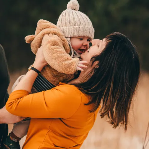 Mama tilt haar baby met wollen mutsje lachend op in het herfstlicht
